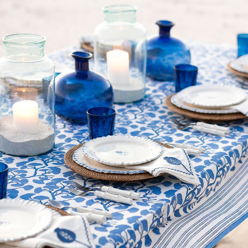 Table setting with blue and white tablecloth, plates, cups, and candles.