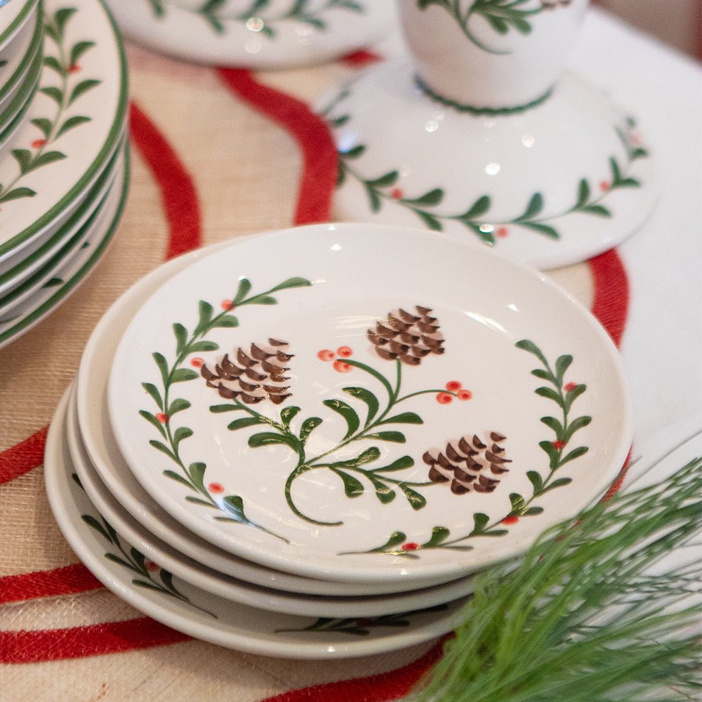 Stack of decorative plates with pine cone and holly design on a striped fabric background