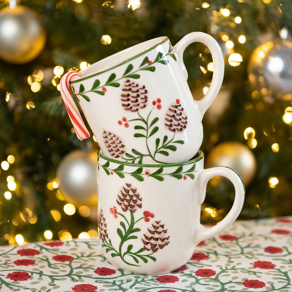 Two stacked mugs with Christmas-themed design in front of a decorated tree.