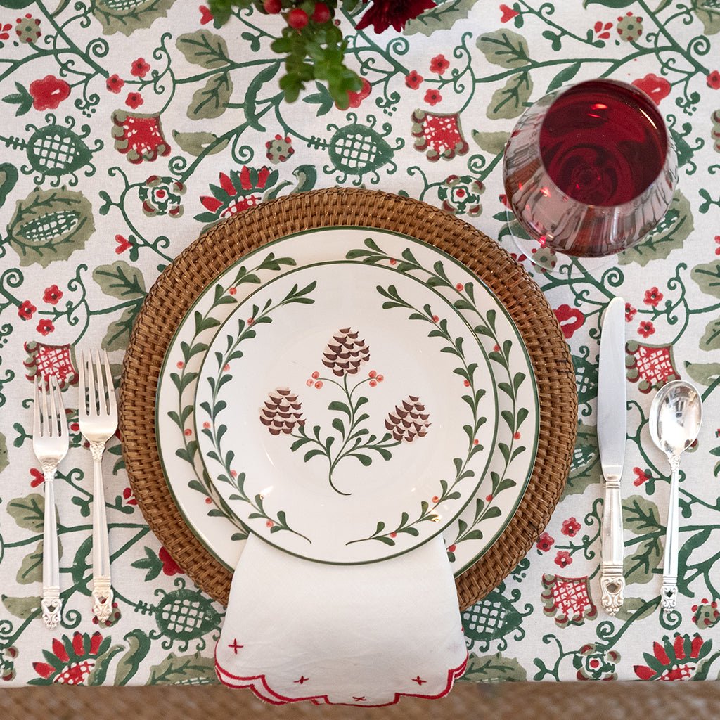 Decorative table setting with floral-patterned plates, cutlery, and a red glass on a matching tablecloth.