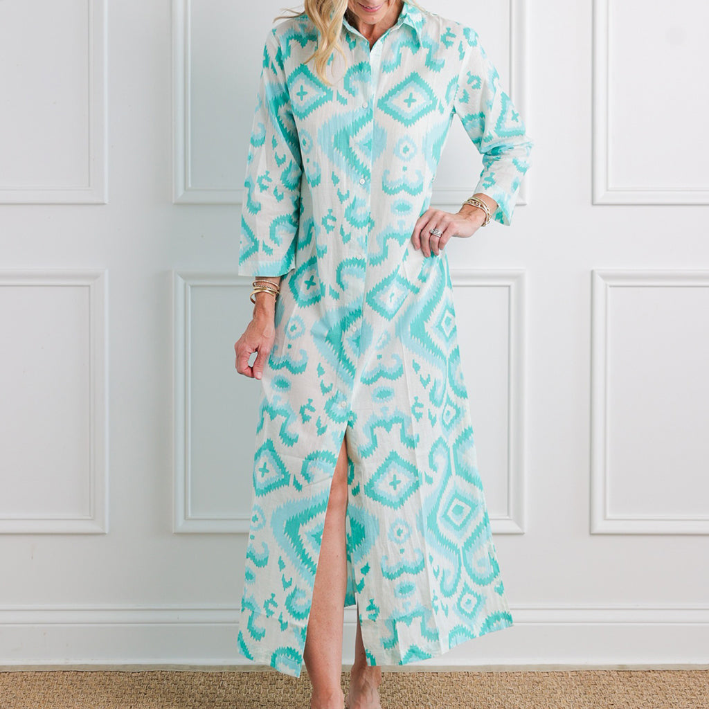 Woman wearing a long, patterned dress with a white wall background