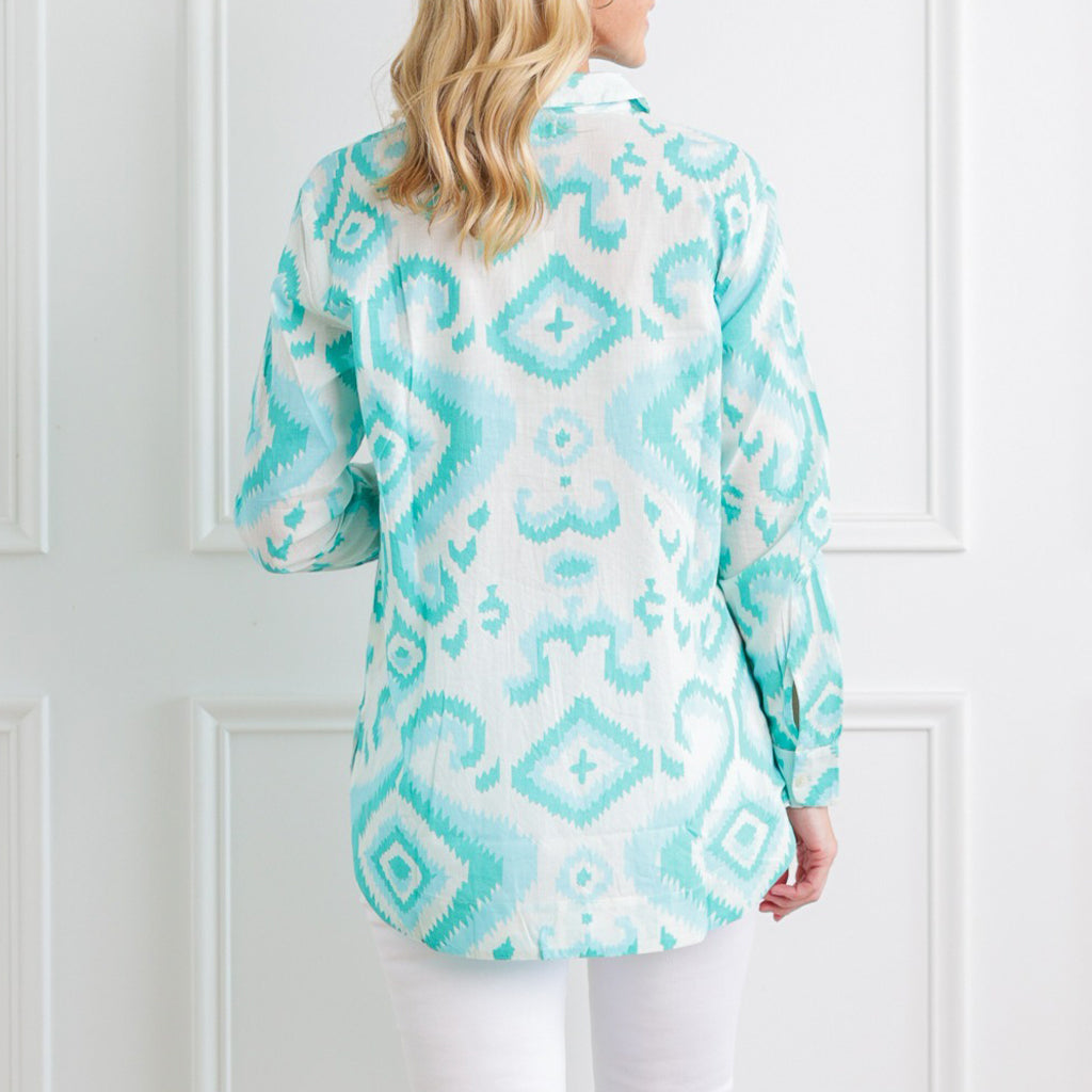 Woman wearing a turquoise and white patterned blouse against a white background