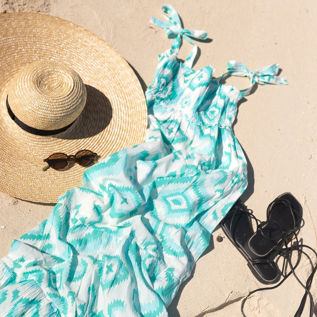 Turquoise patterned dress with a straw hat and sunglasses on sand