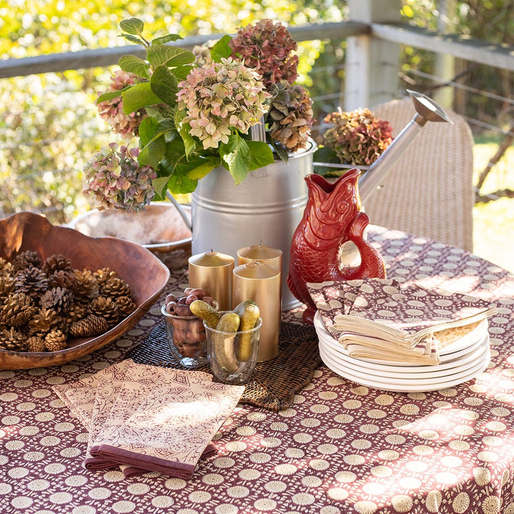 Decorative table setting with flowers, candles, and a red fox figurine on a patterned tablecloth.