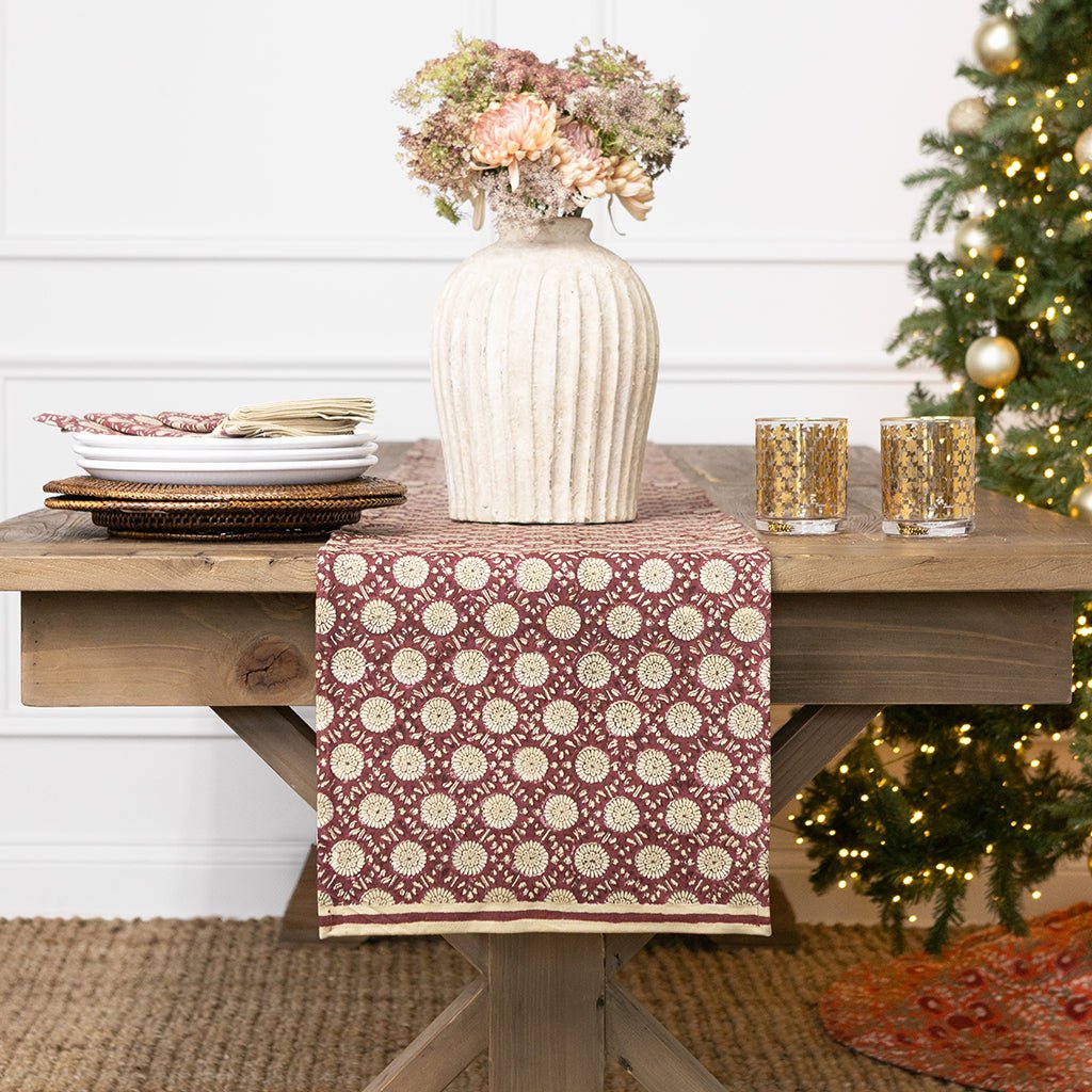 Decorative table setting with a patterned table runner, vase with flowers, and candles on a wooden table.