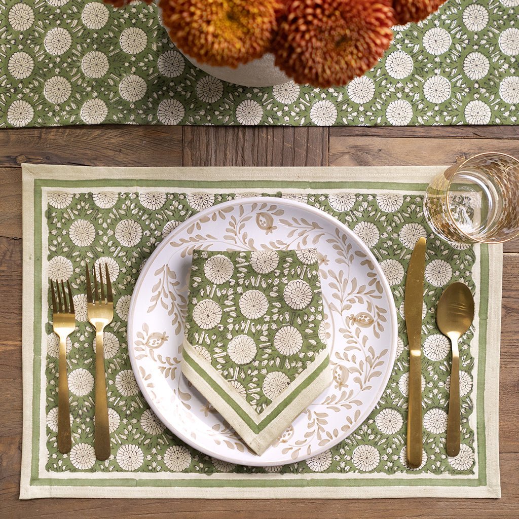 Table setting with green and white patterned placemat, plate, and napkin on a wooden table.