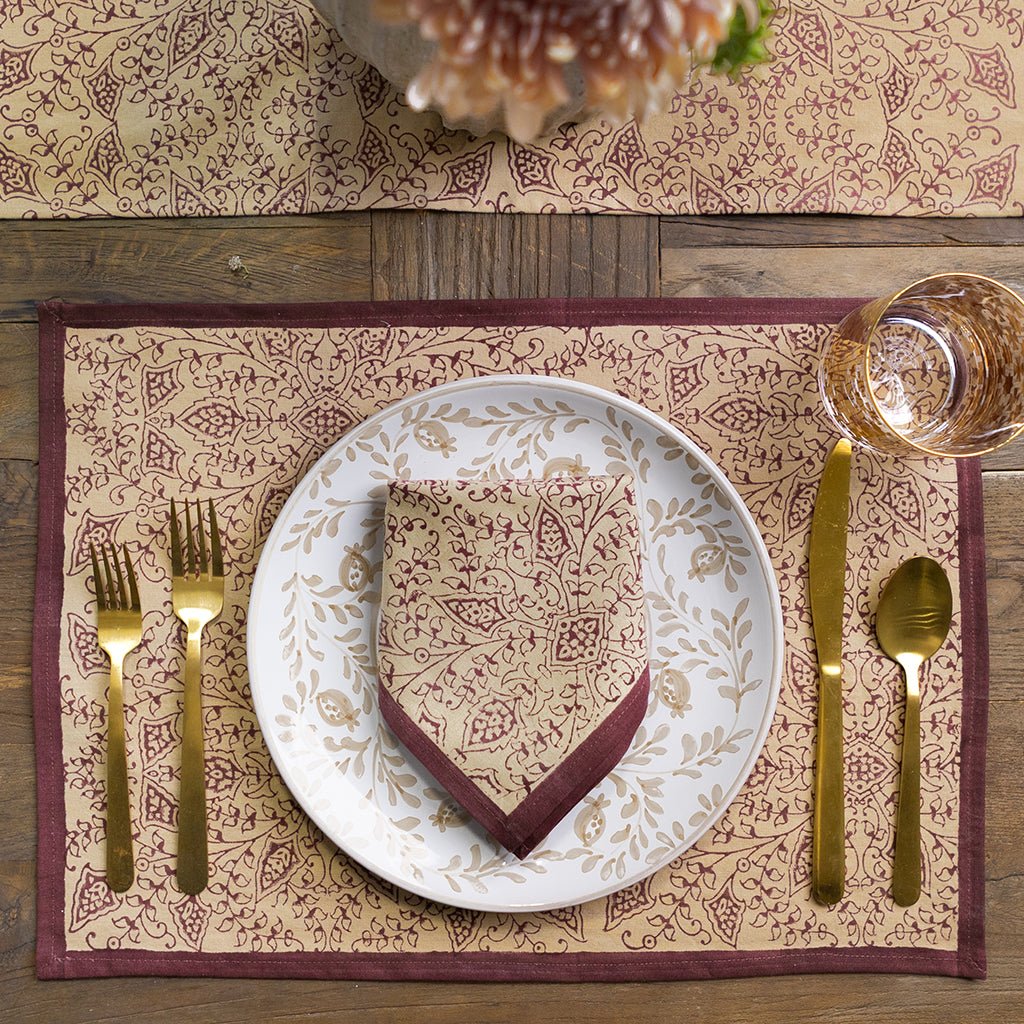 Dining table setting with patterned placemat, plate, and cutlery on a wooden surface.