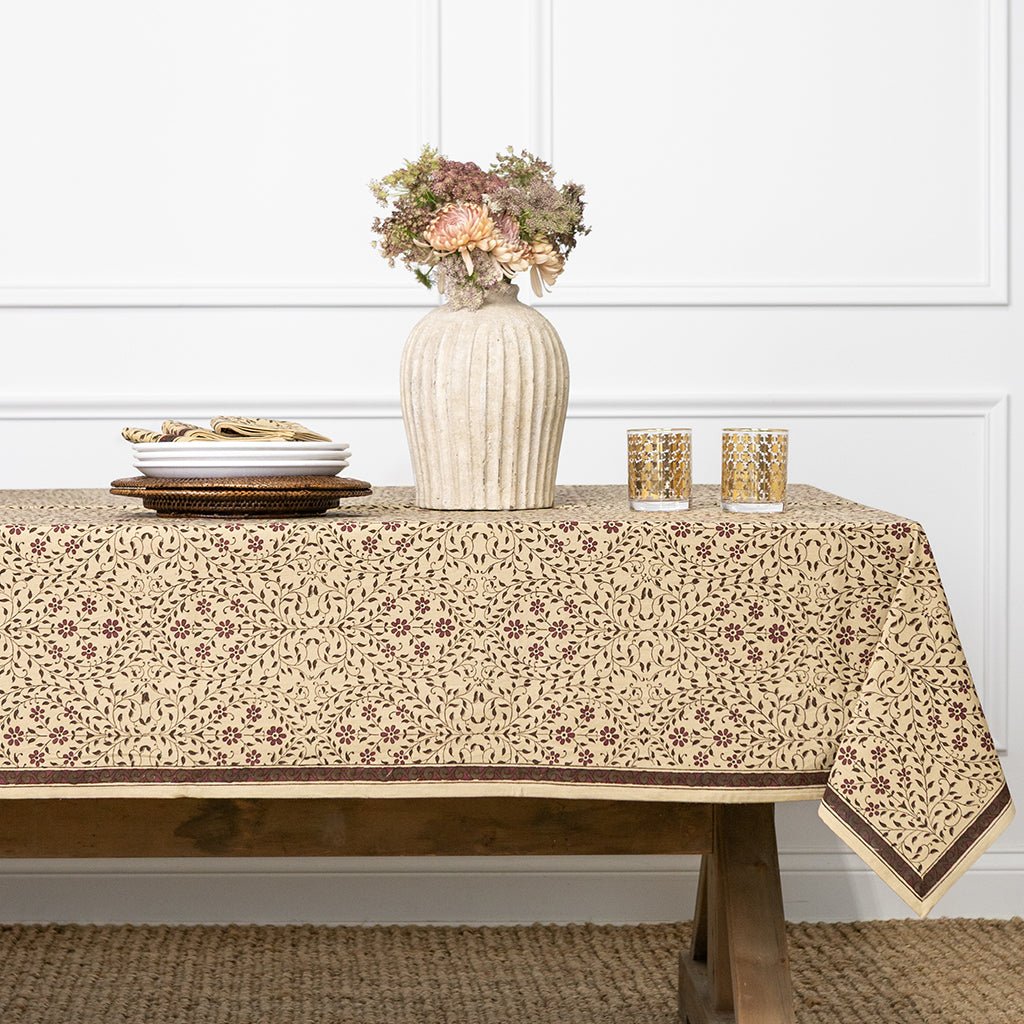 Tablecloth with floral pattern on a wooden table against a white paneled wall.
