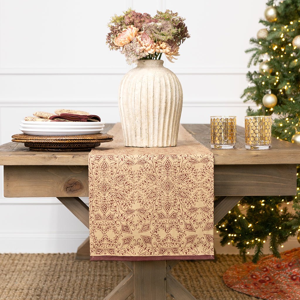 Decorative table setting with a vase, plates, and glasses on a wooden table in front of a Christmas tree.