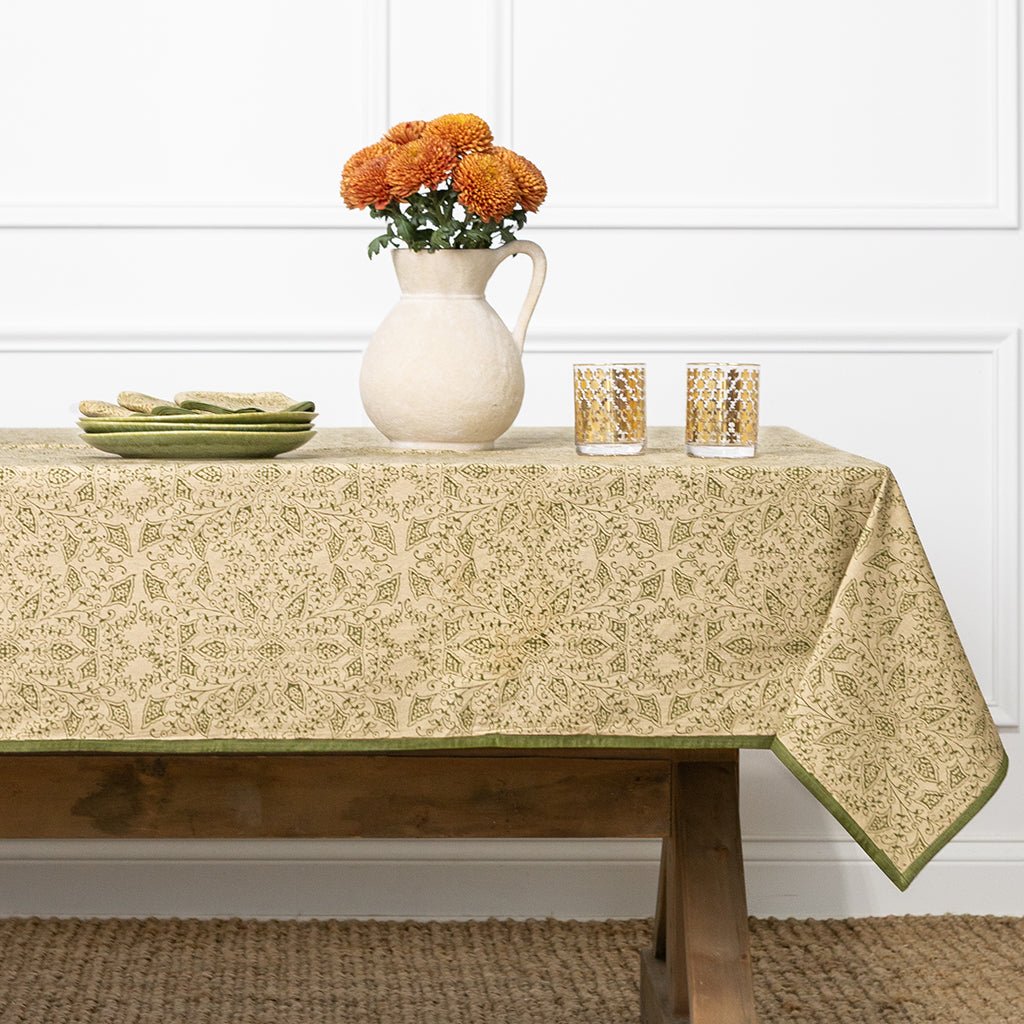 Tablecloth with floral pattern on a wooden table with a vase of flowers and glasses.