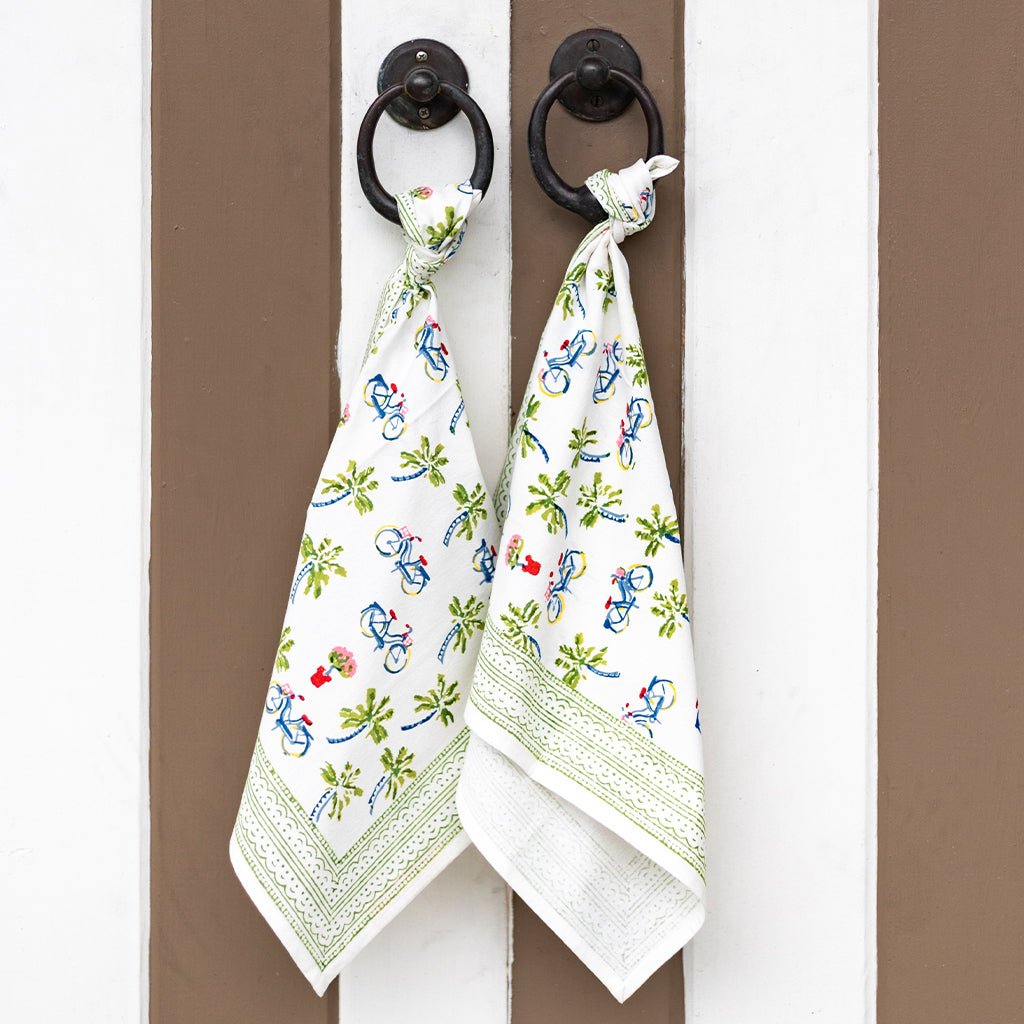 Two white napkins with colorful designs hanging on a door handle.