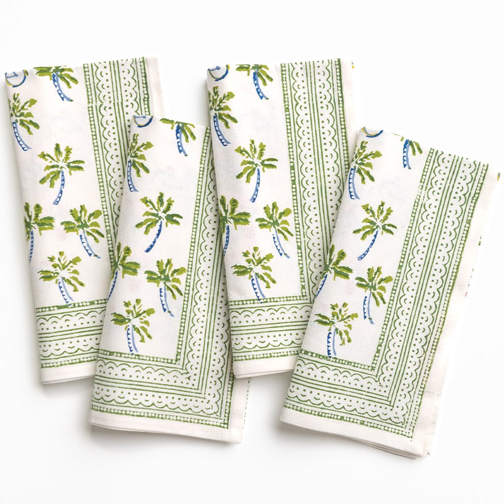Set of four white napkins with green leaf patterns on a white background