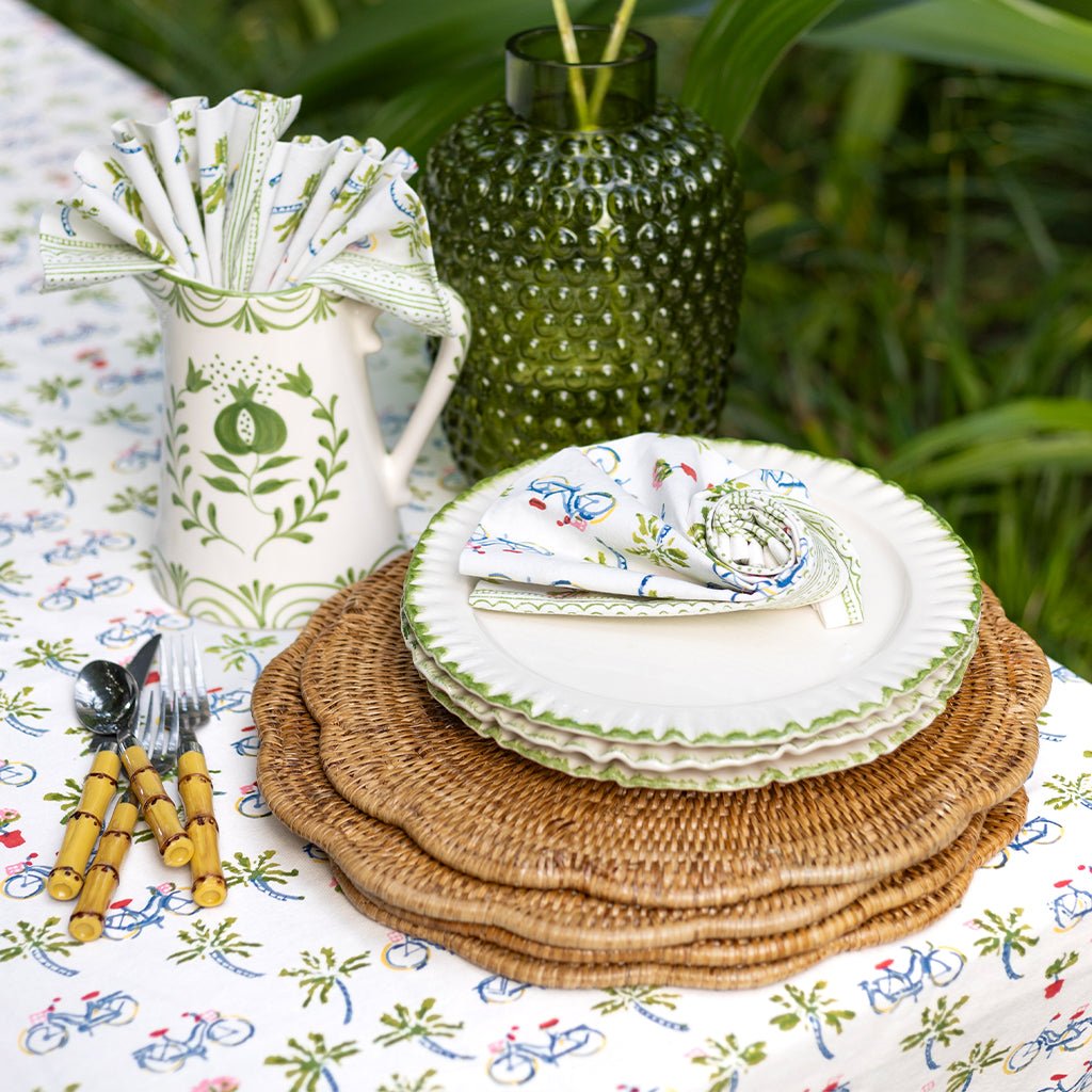 Dining table setting with plates, napkins, and cutlery on a patterned tablecloth outdoors.