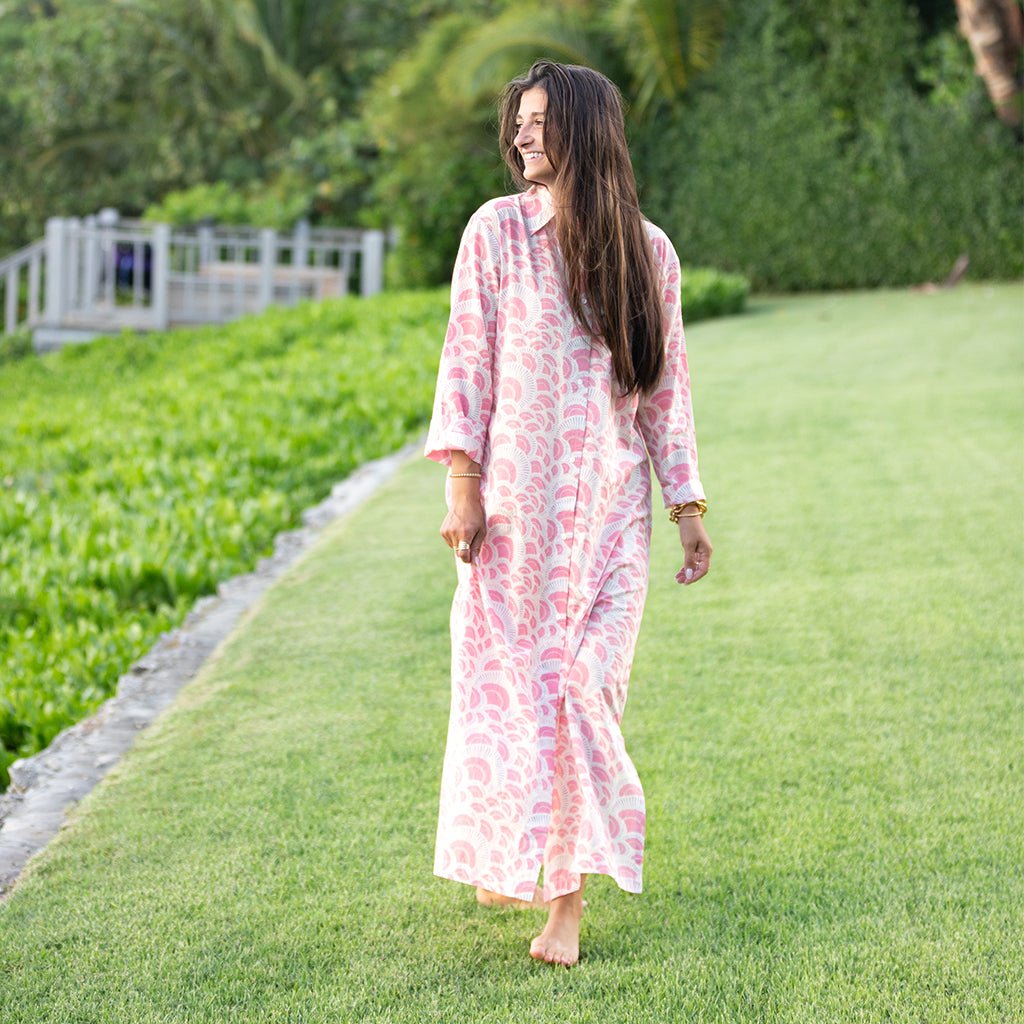 Woman in a long, light-colored dress standing on grass with greenery in the background