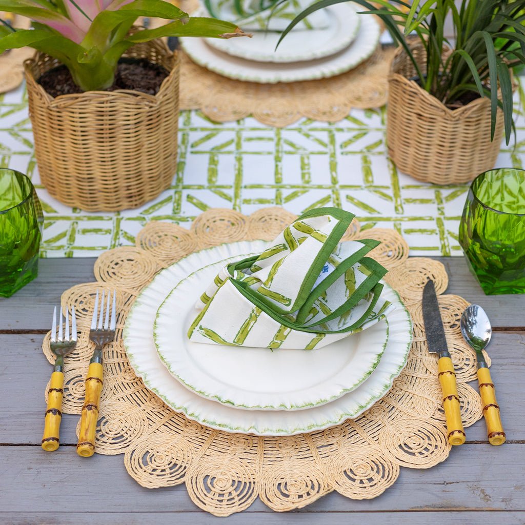 Table setting with white plates, green napkins, and decorative placemats on a wooden table.