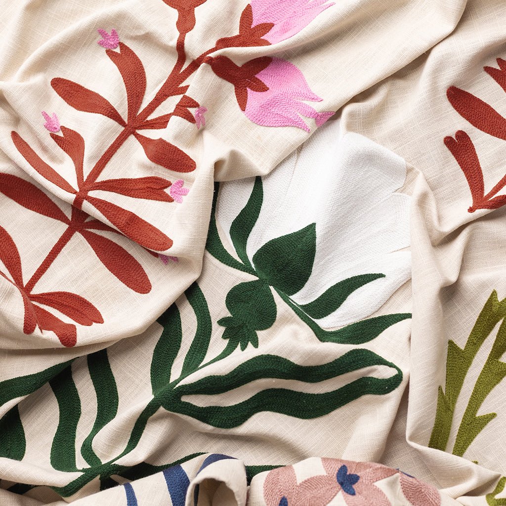 Close-up of fabric with floral patterns in red, green, and pink on a beige background.