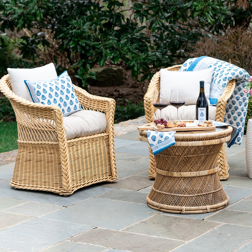 Two wicker chairs with cushions and a small table on a stone patio with outdoor setting.