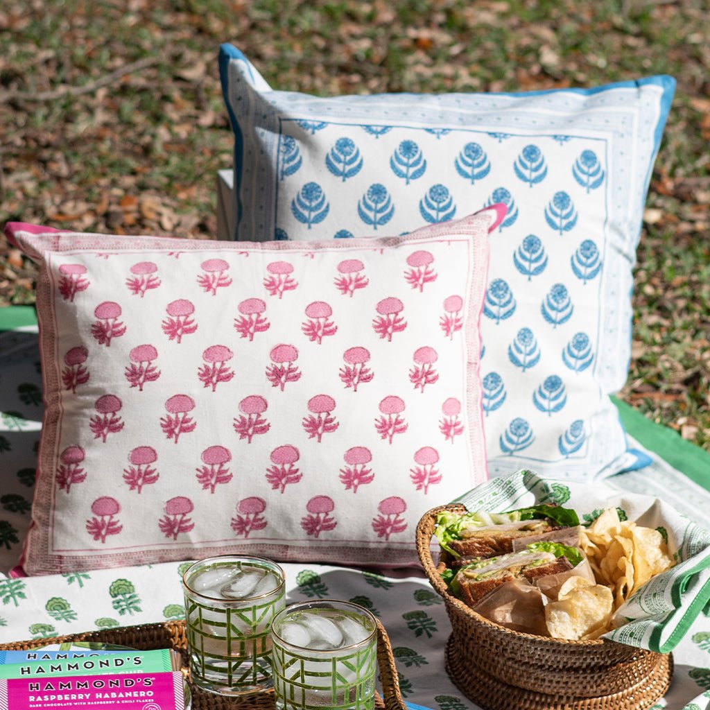 Two patterned pillows on a quilt with snacks and drinks outdoors.
