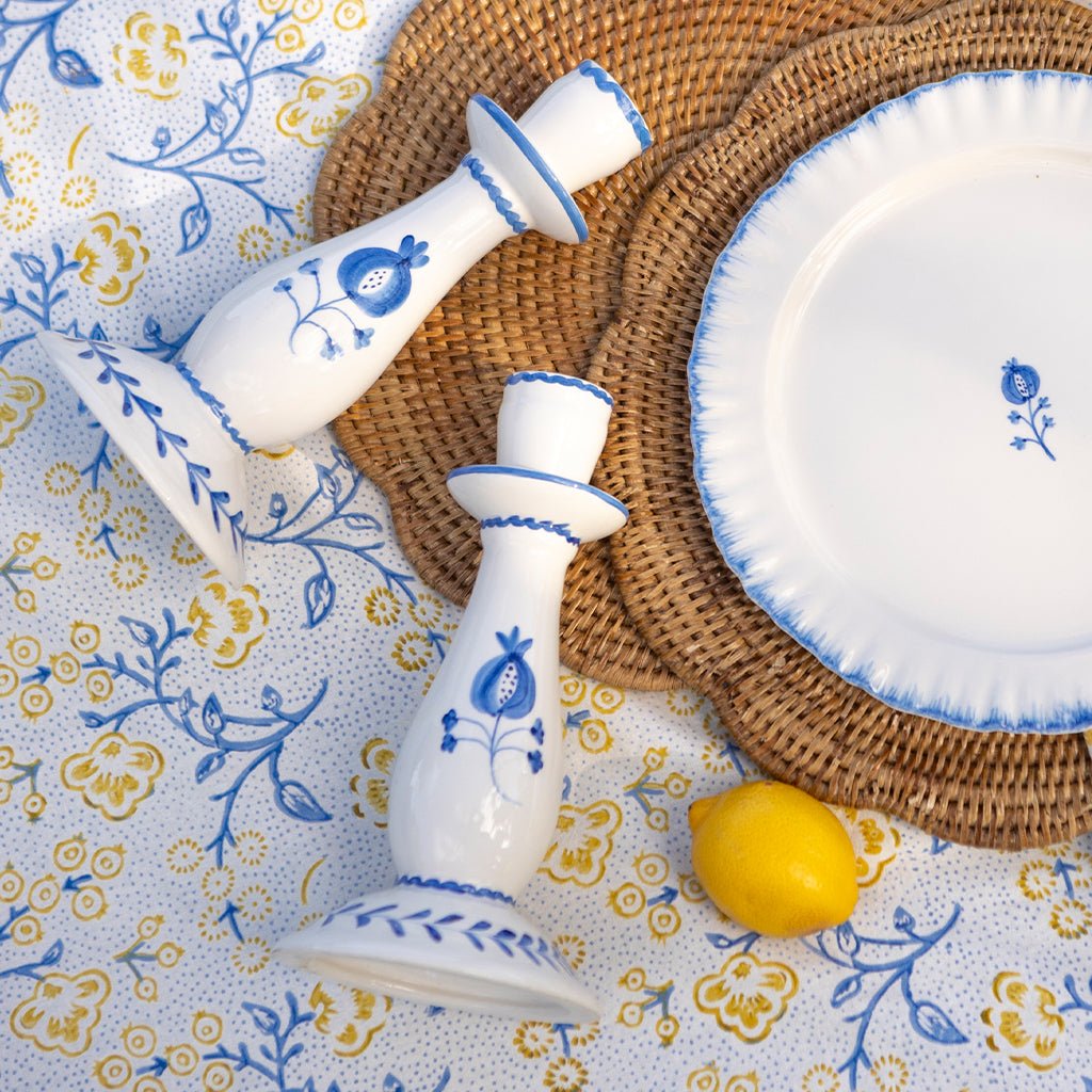 White ceramic candle holders with blue floral patterns on a decorative tablecloth.