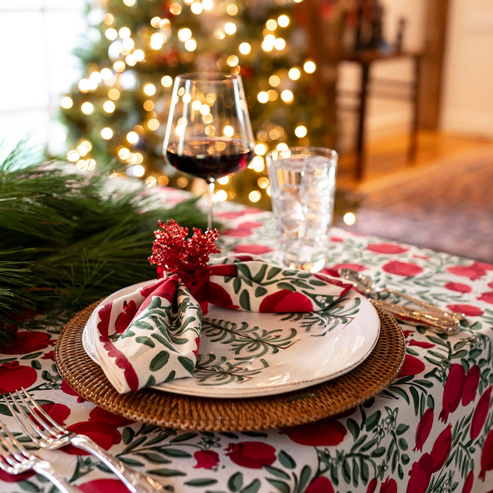 A Christmas table setting featuring pomegranate napkins and a tablecloth.