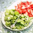 A decorative green and white platter with fruit on a green patterned tablecloth.