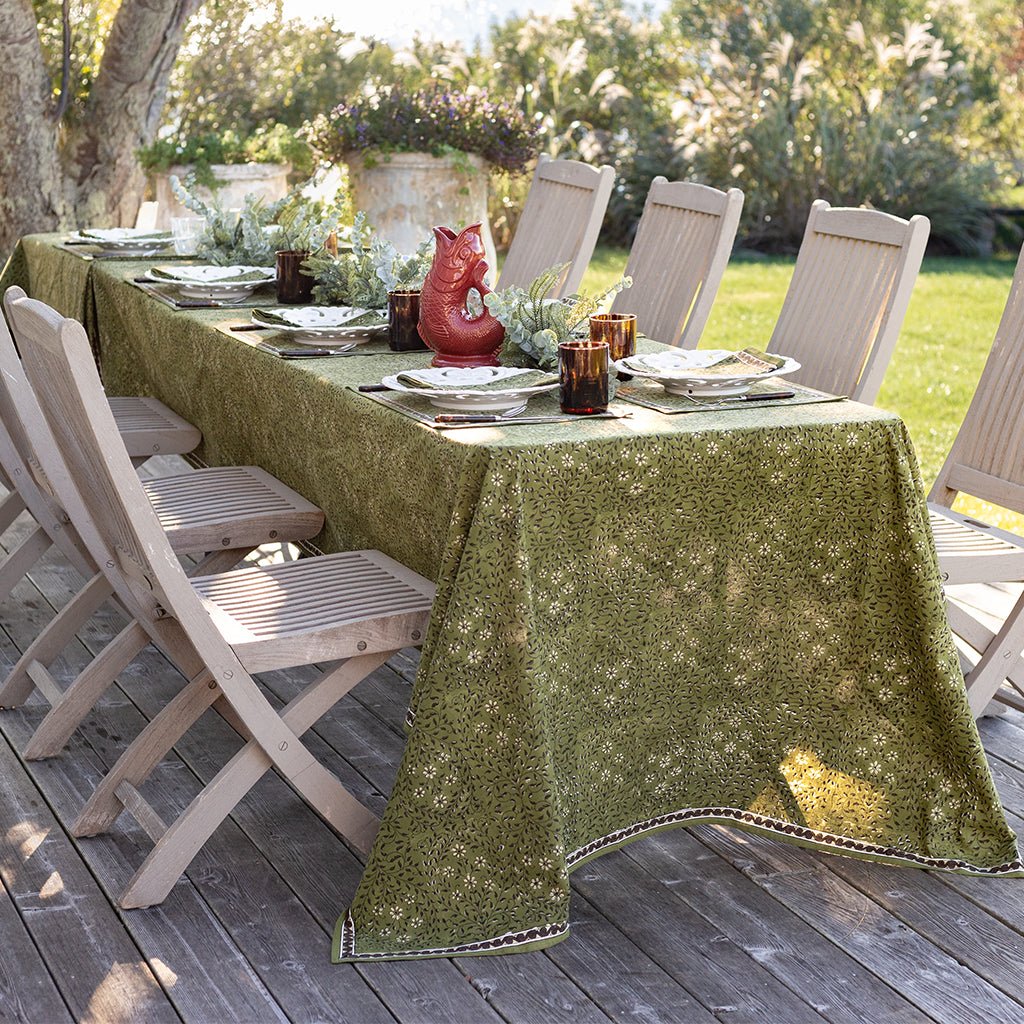 Outdoor dining setup with a green patterned tablecloth on a wooden deck.