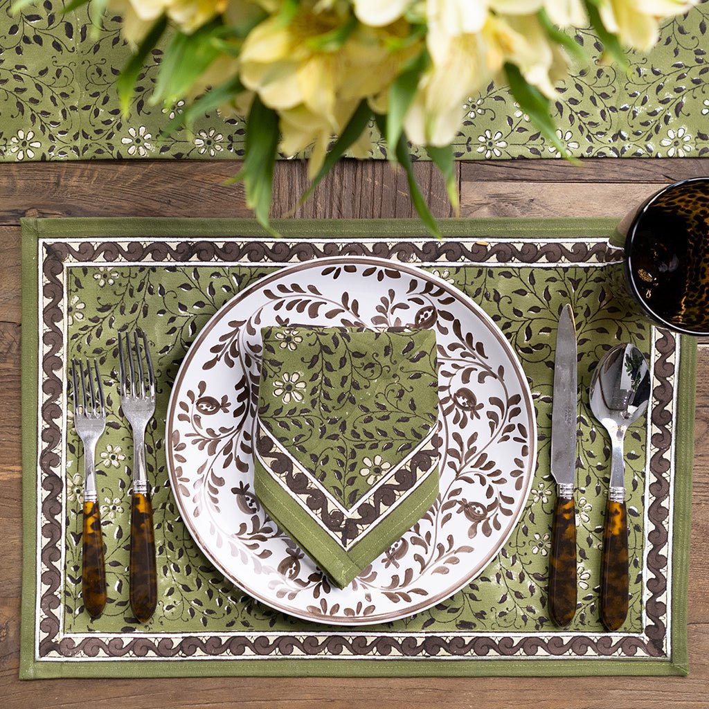 Decorative table setting with a plate, cutlery, and napkin on a green patterned placemat.