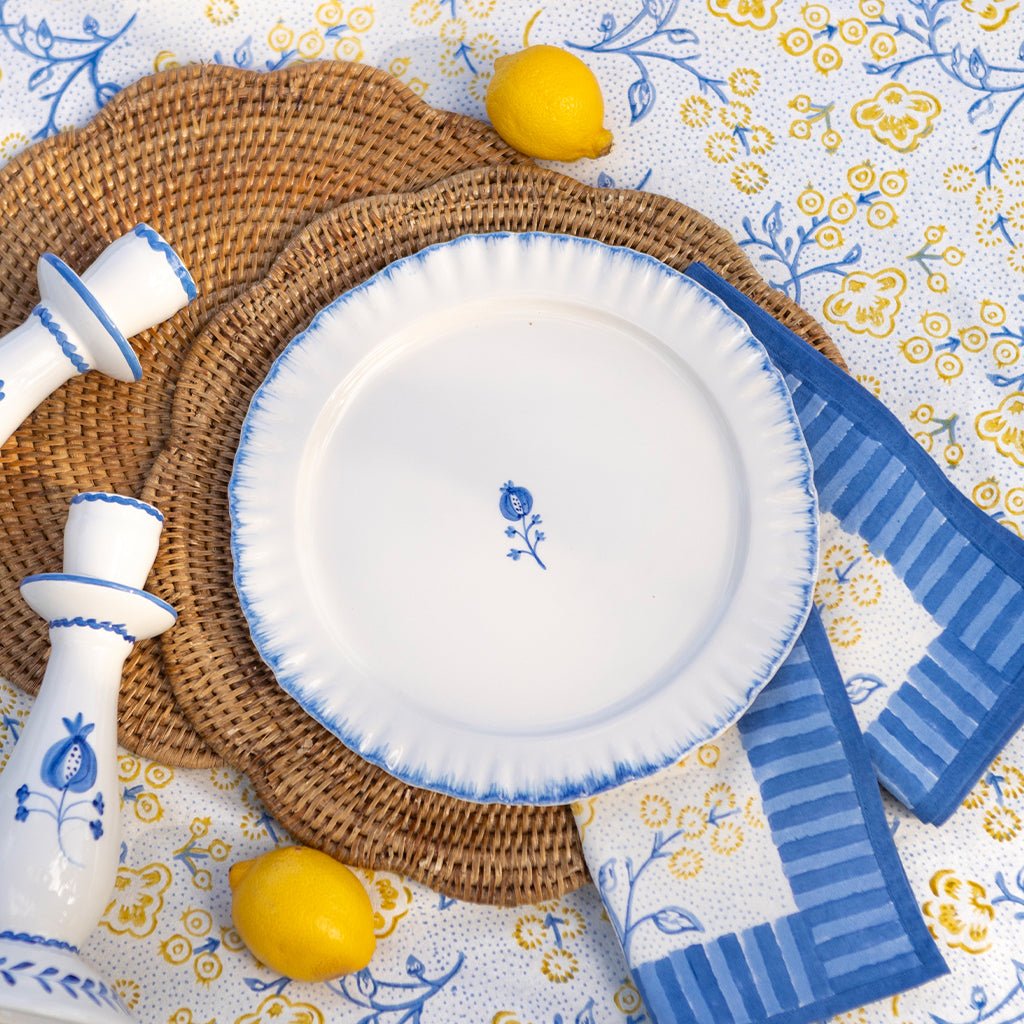 White plate with blue rim and floral design on a patterned tablecloth with lemons and striped napkins.
