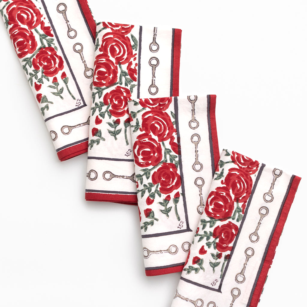 Set of four napkins with red rose pattern and snaffle bit border on a white background.