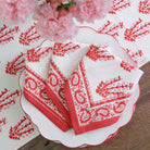 A set of folded Sagar red and white napkins with a hand block-printed design, displayed on a white plate with a floral pattern.
