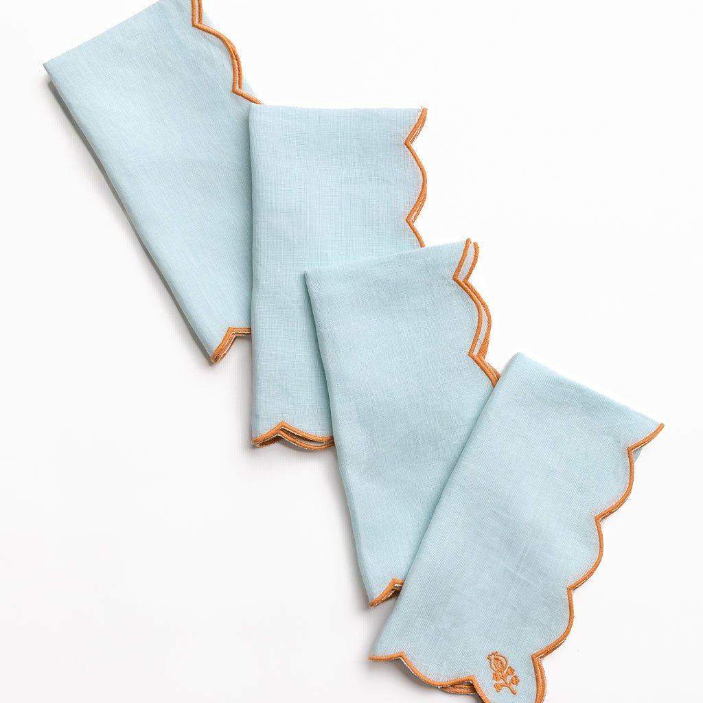 Set of four light blue napkins with orange scalloped edges on a white background