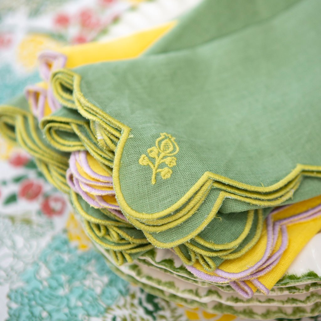 Stack of green napkins with yellow trim and floral embroidery on a floral fabric background