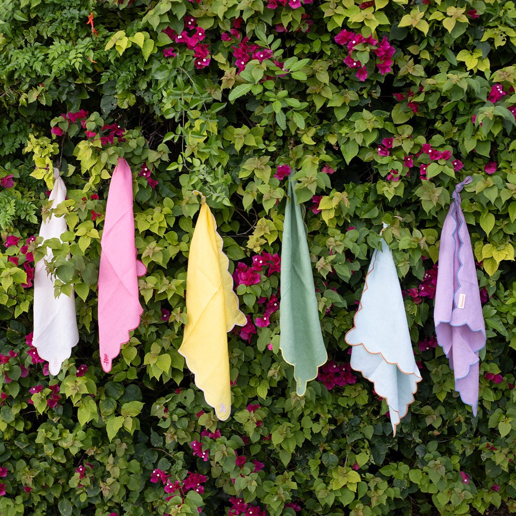 Colorful cloths hanging against a green leafy background with pink flowers