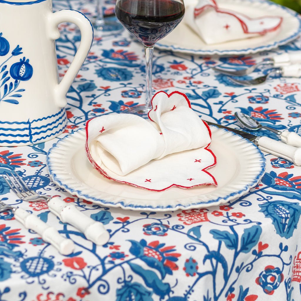 Dining table setting with floral tablecloth, plates, cutlery, and a glass of red wine.