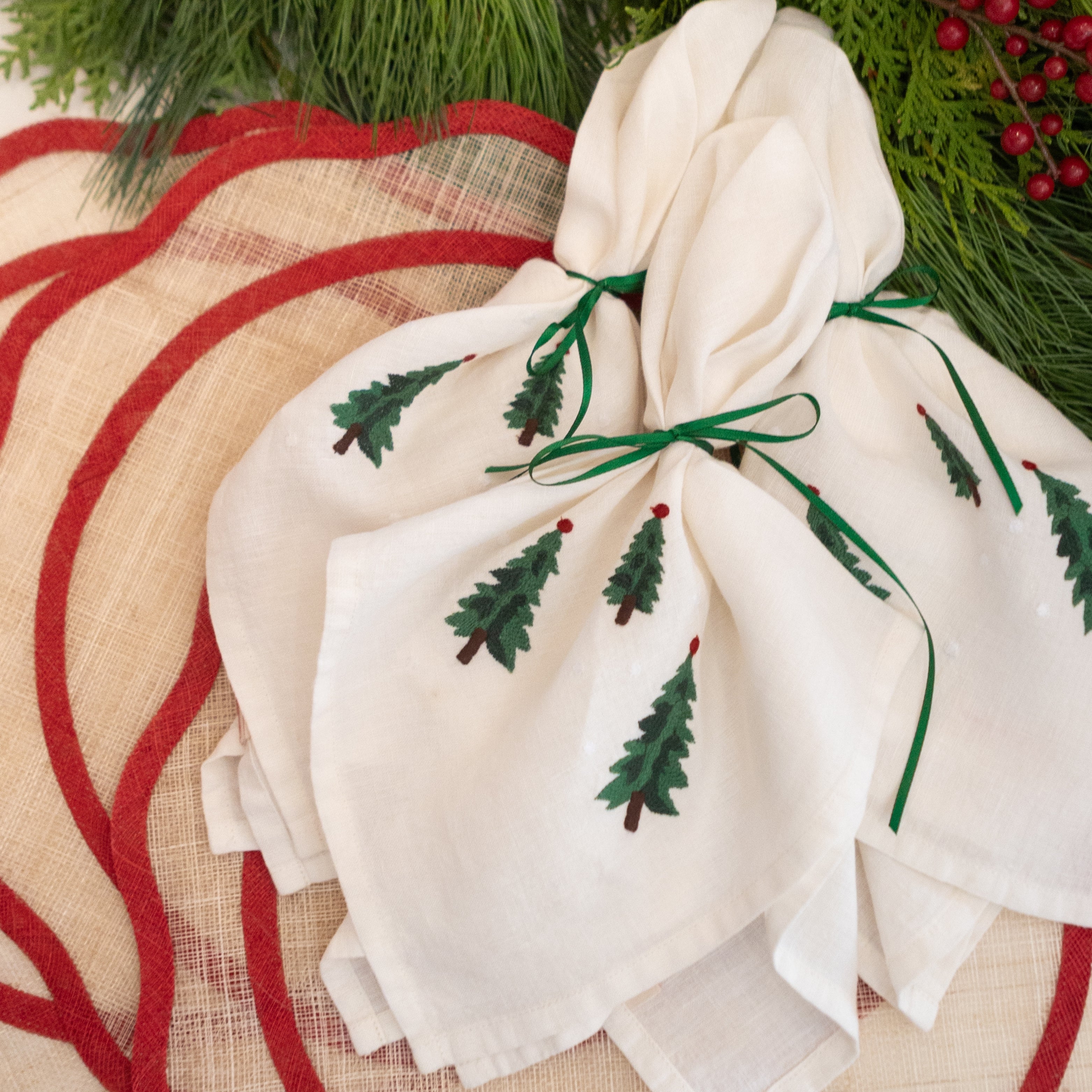White fabric with embroidered green trees on a red and beige placemat