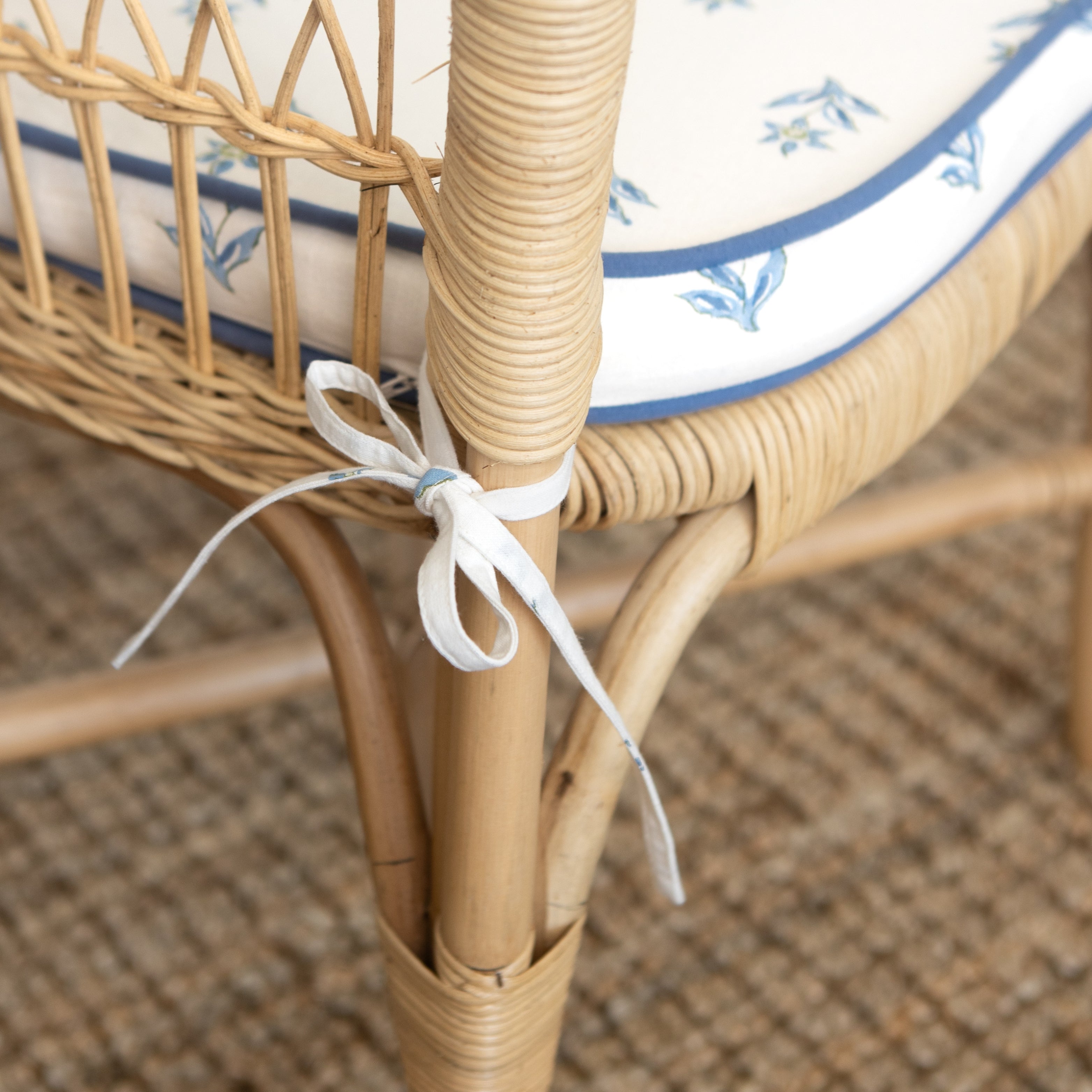 Close-up of a wicker chair with a decorative ribbon tied around the leg.
