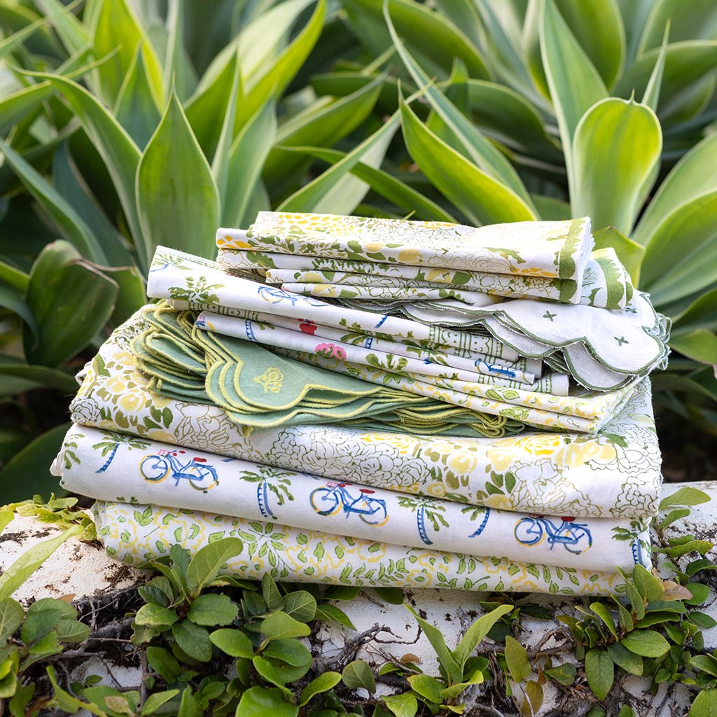 Stack of patterned linens on a stone surface with green plants in the background