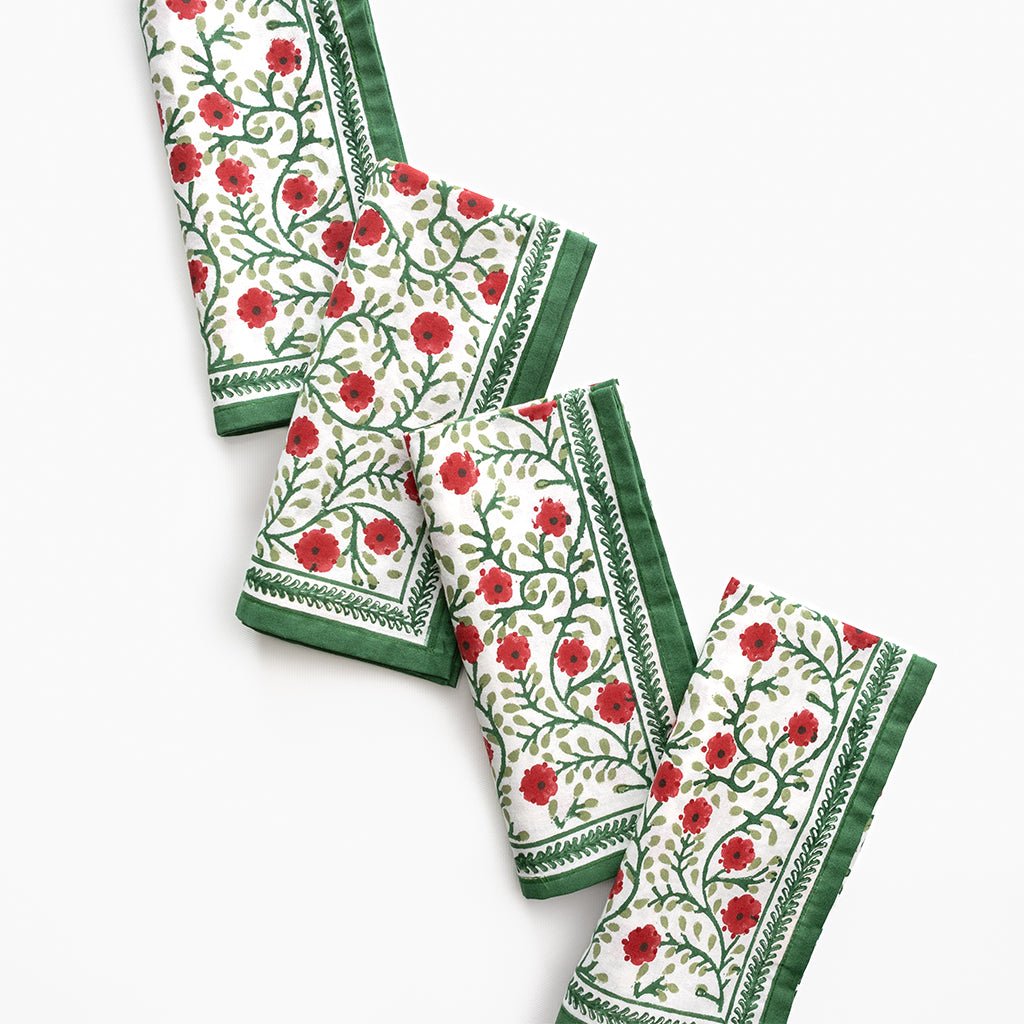 Set of four floral patterned napkins with red flowers and green borders on a white background