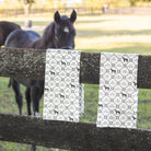 Two tea towels with horse pattern hanging on a wooden fence, with a horse in the background.