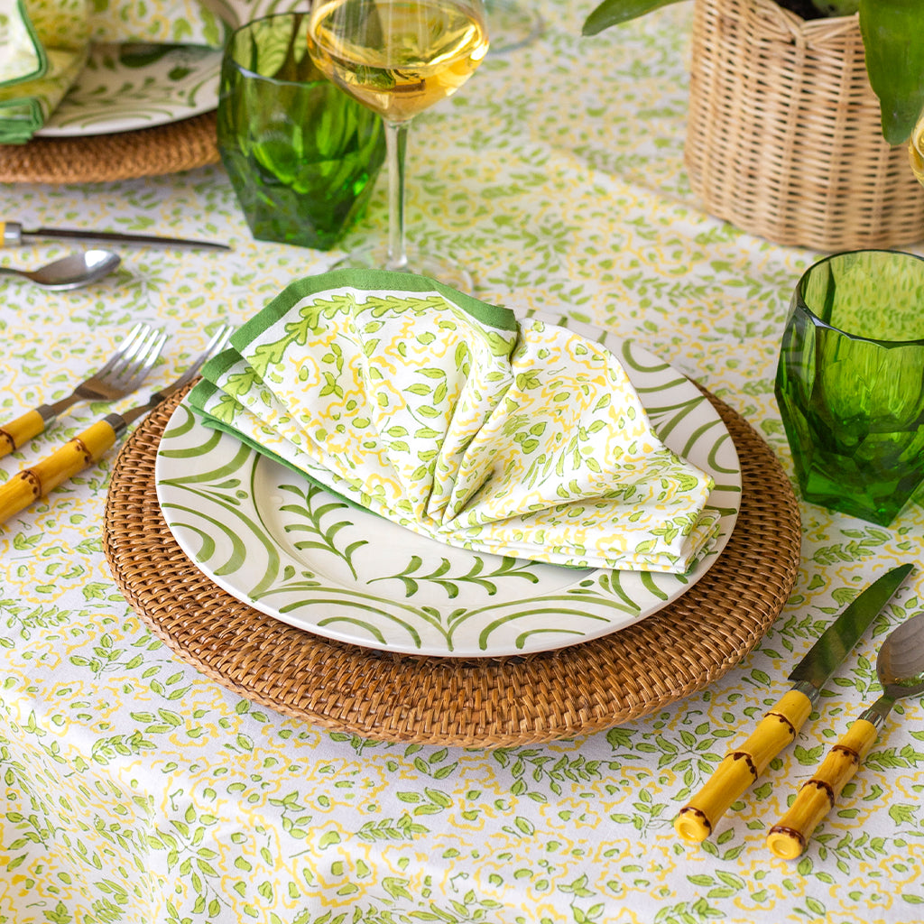 Dining table setting with green and white patterned plates, napkins, and glasses.