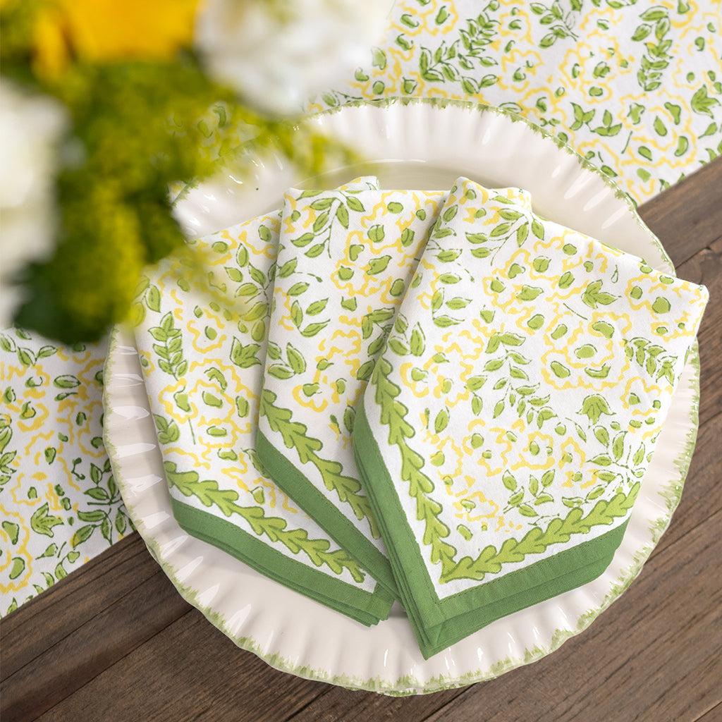 Stack of green and white patterned plates on a wooden surface with blurred flowers in the background.