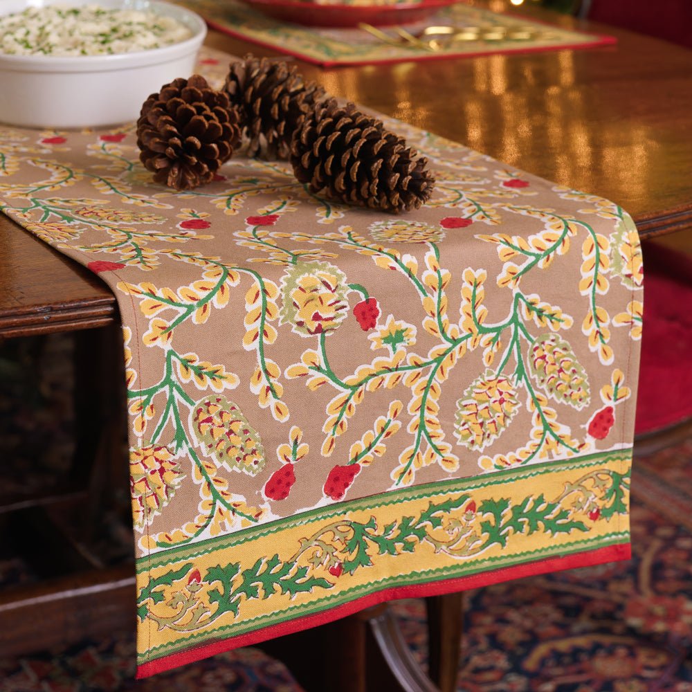 A table runner with a pinecone motif on a wooden table layered with pinecones