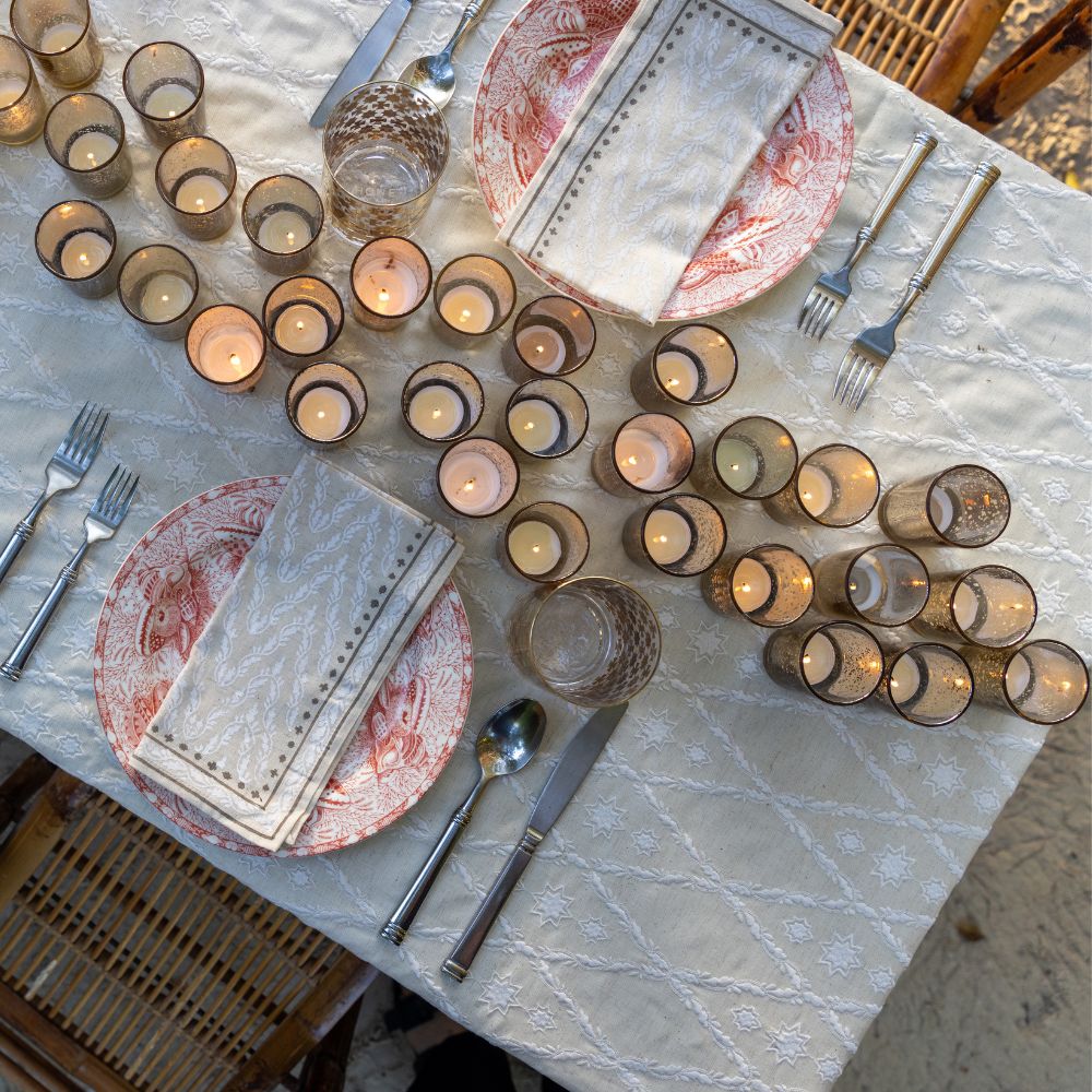 An ivory tablecloth with an embroidered diamond pattern on a dining table set with dishes and cutlery.
