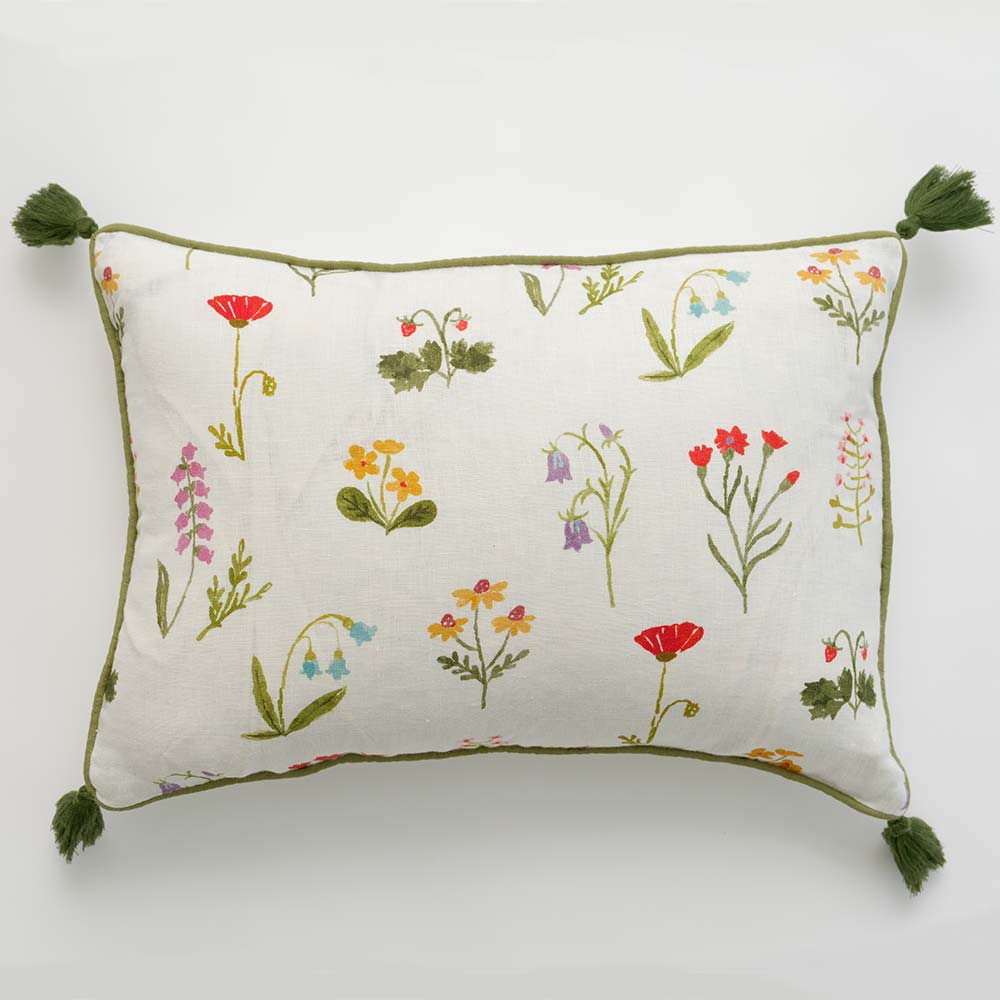Pillow cover with red poppy flowers, mini yellow daffodils, and lavender bluebells on a soft white linen base with green outline detailing and pom poms.