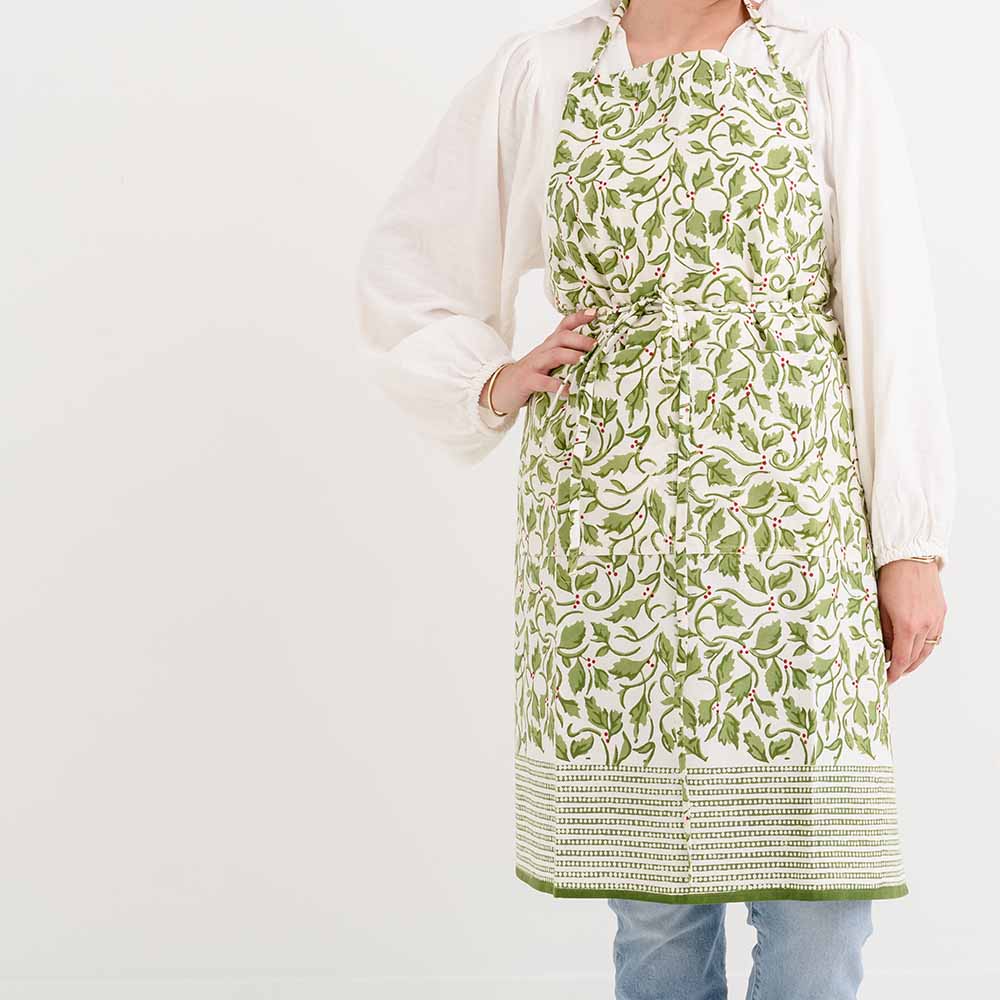 A person wearing a green apron with a Christmas holly and berries pattern.