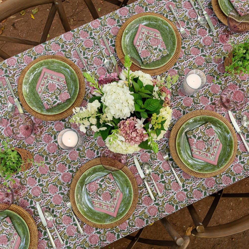 overhead view of table with bohemian floral moss & mauve tablecloth with matching napkins on green plates and wicker chargers
