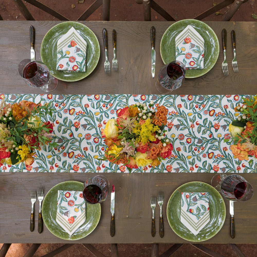 table runner with floral pattern in shades of sage green, crimson, marigold and deep orange with matching napkins folded on green plates