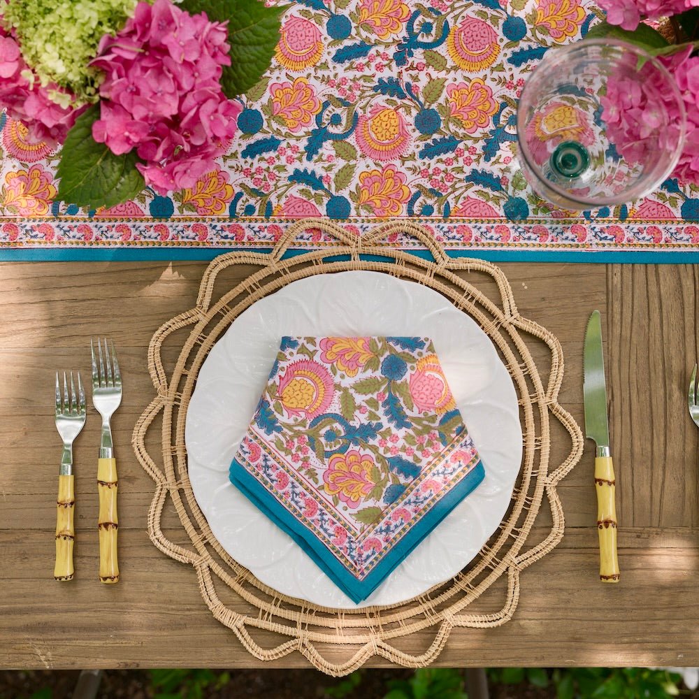 Jewel tone colored napkin with blossom design folded on white plate.