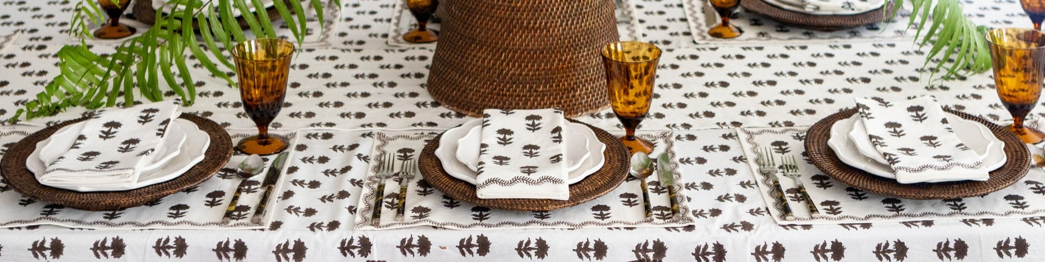 A tablesetting with a white and brown tablecloth and napkins and woven table accents