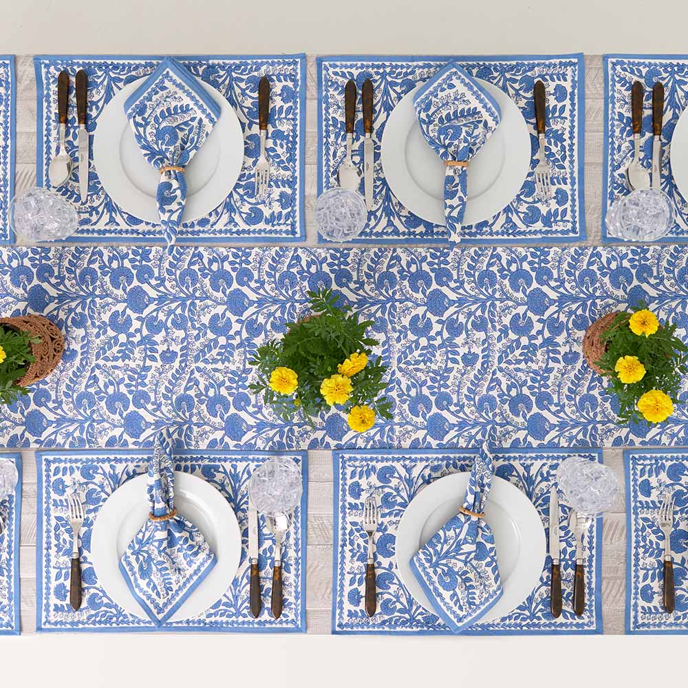Set of blue and white patterned placemats with cutlery and plates on a white table.